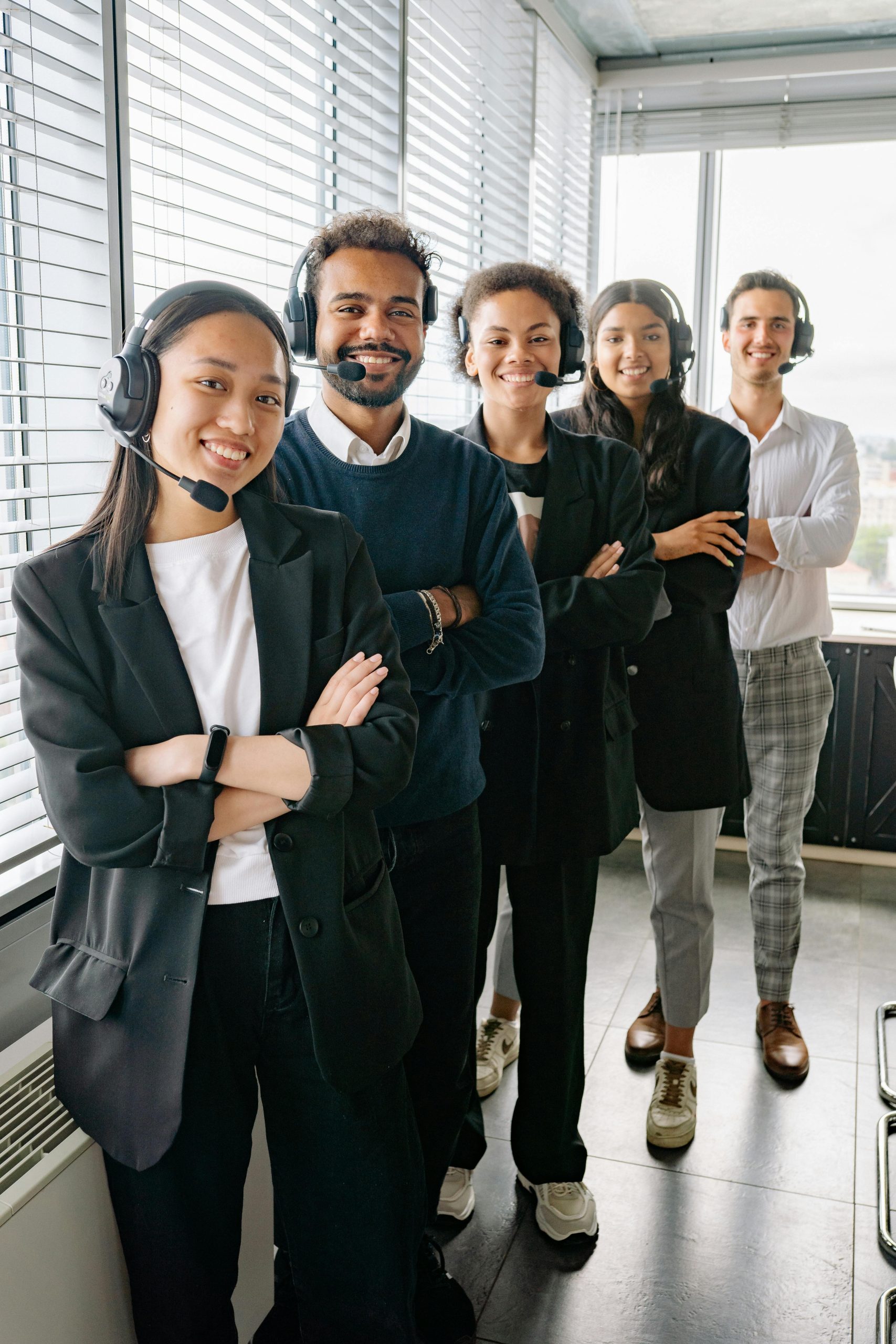 Diverse group of call center professionals wearing headsets, standing confidently in an office.